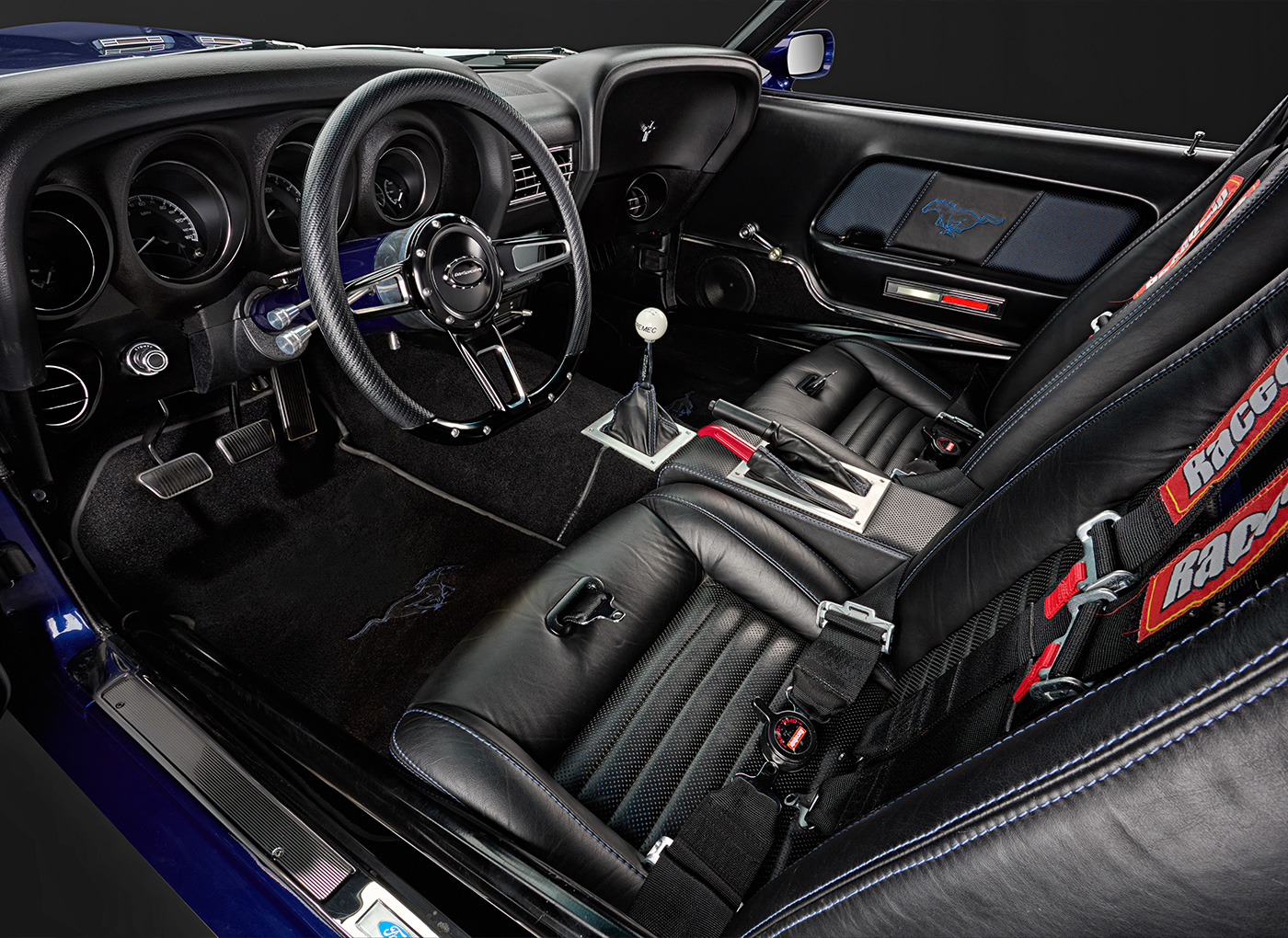 Inside of a mustang featuring black leather seats, racing seatbelts, and a blue embroidered Mustang